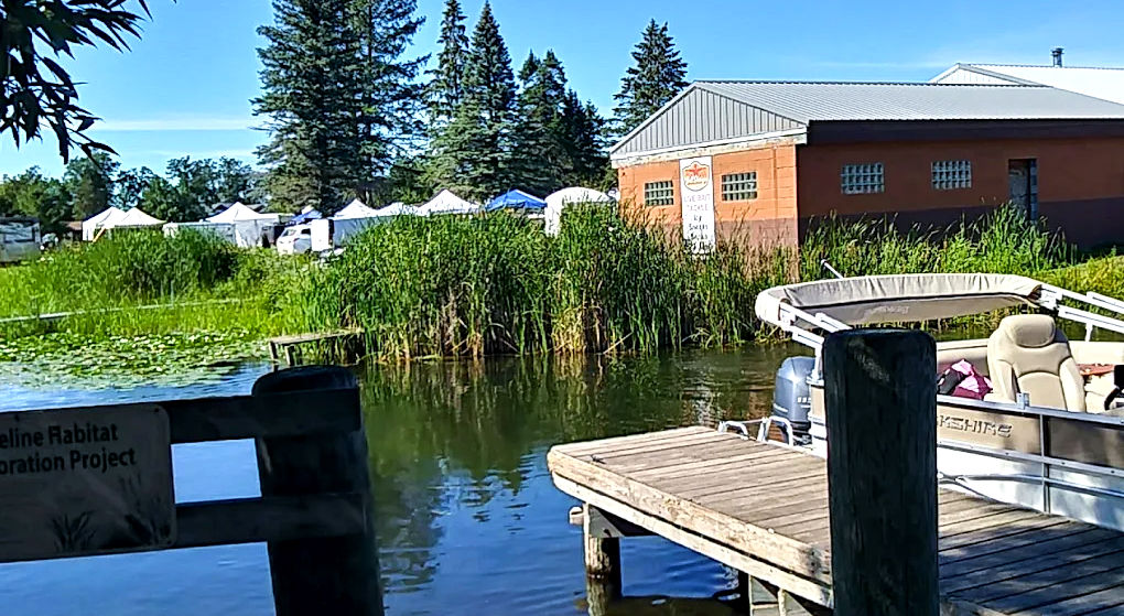 Dock and boat on the lake with trees and building in the background. City of Longville.