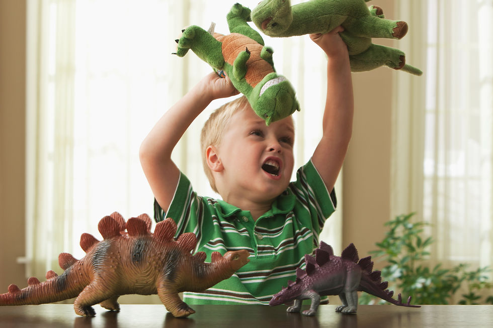 Child in a striped green shirt joyfully playing with toy dinosaurs on a table. Bright, sunny room with soft light and potted plant in background.