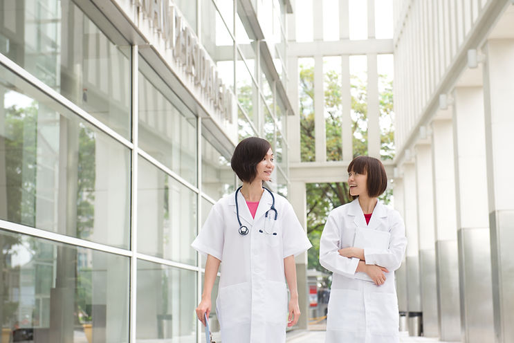 Two healthcare practitioners are having a discussion while walking through a windowed corridor.