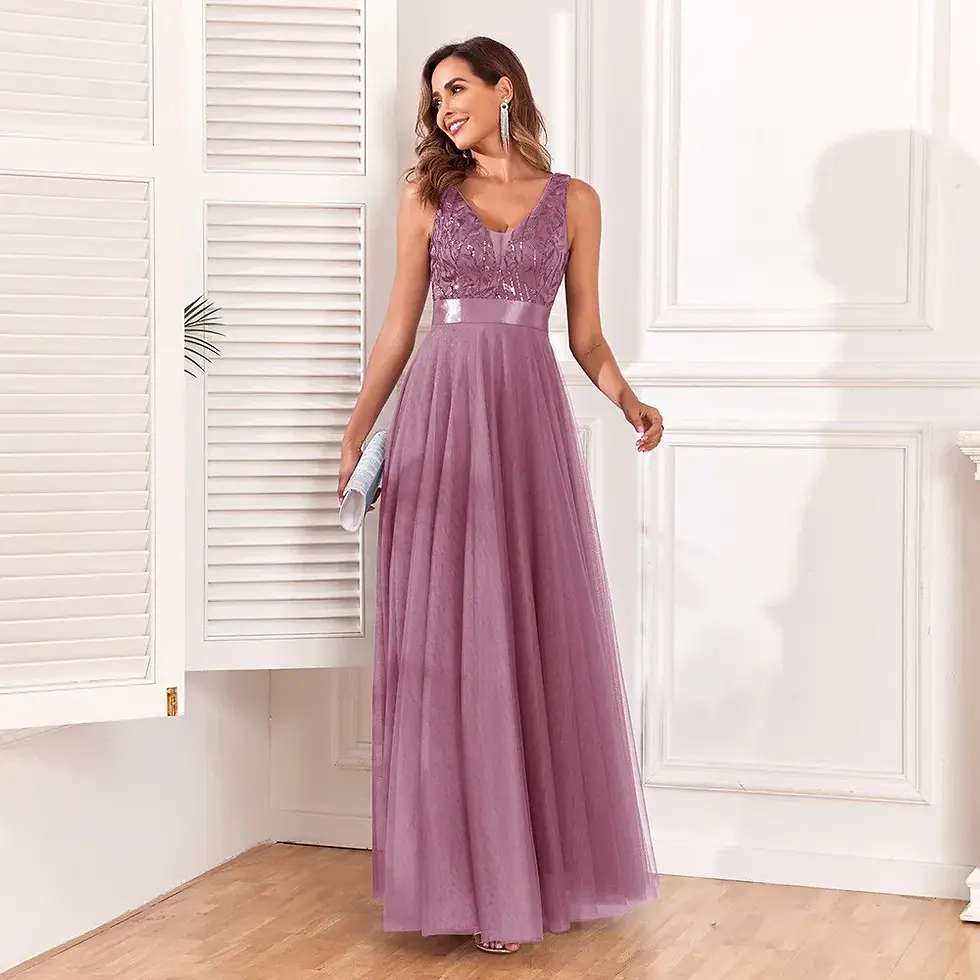 Thumbnail: Woman wearing a sleeveless pink bridesmaid dress with lace detail, posing in a white room and looking over her shoulder.