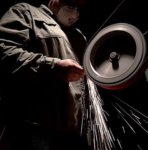 Maker grinding a blade on a belt grinder throwing sparks