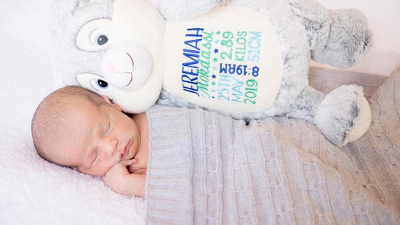 Sleeping newborn wrapped in a grey blanket next to a custom embroidered birth stats grey plush toy animal.