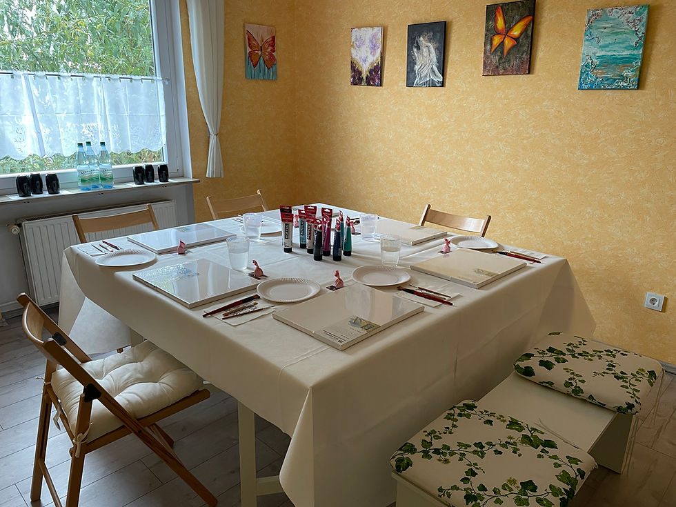 Das Atelier in Weiterstadt: Ein gedeckter quadratischer Tisch, auf dem Pinsel, Paletten und Leinwände angerichtet sind.