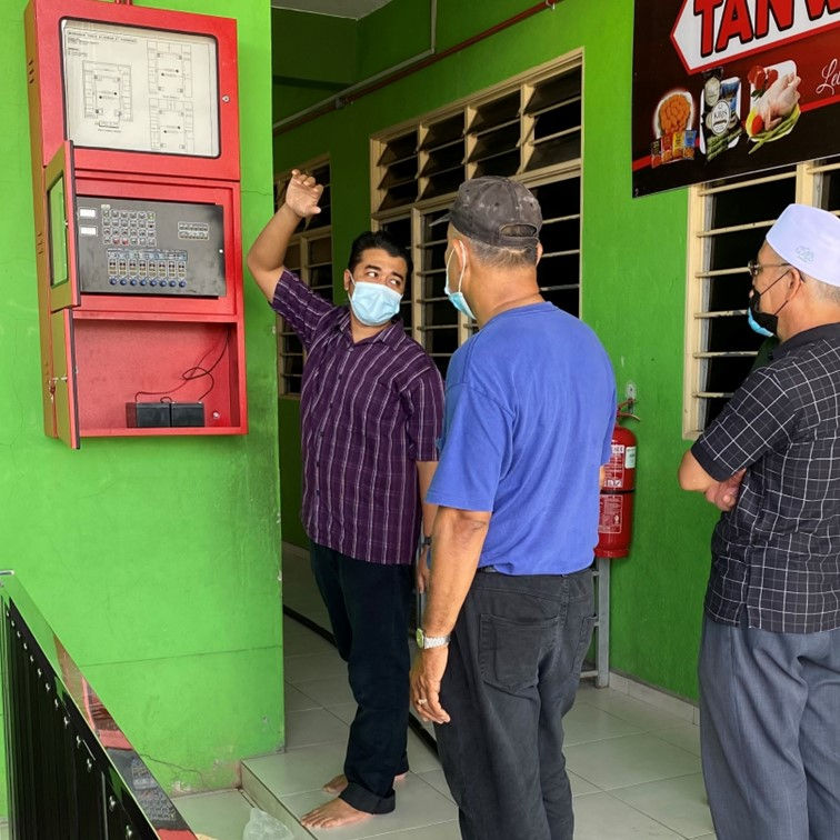 Discussion on Fire Safety: A technician explains the operation of a fire protection system to two individuals inside a brightly painted building, emphasizing the importance of safety measures.