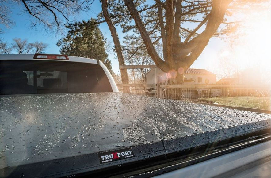 Wet truck bed with "Truxport" logo glistens in sunlight. Tree and house in background, creating a serene morning mood.