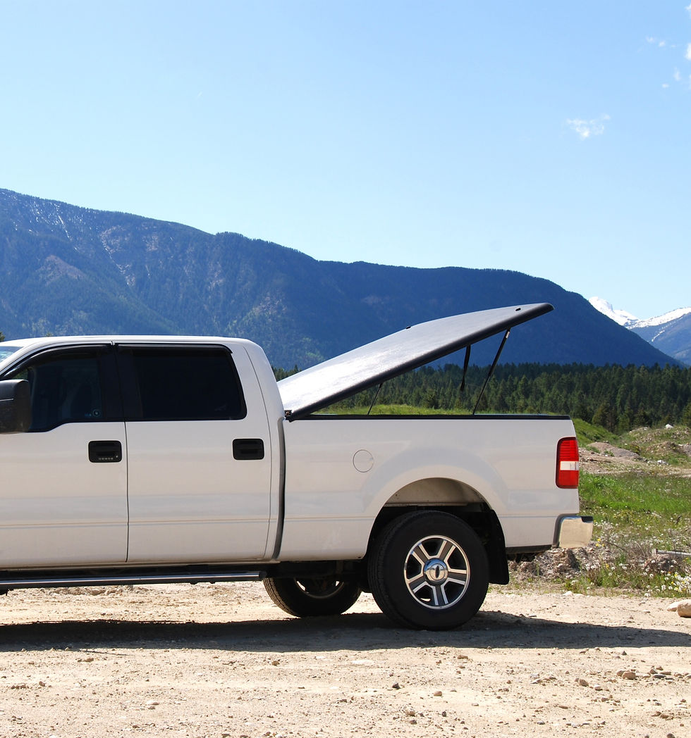White pickup truck with open tonneau cover in a scenic mountain setting. Bright blue sky and greenery enhance the calm, outdoor mood.