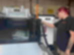 Woman in a workshop inspects a truck liftgate, with metal racks, straps, and tools around her.