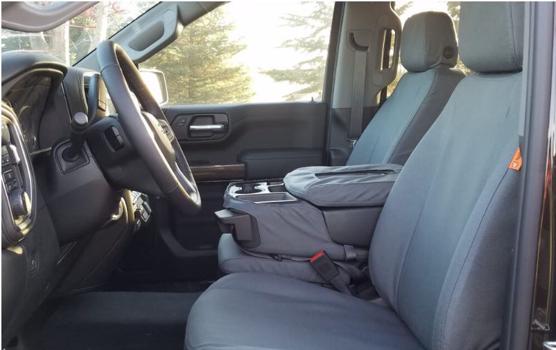 Empty truck interior with gray fabric seats, a central armrest, and a visible steering wheel. Trees are seen through the sunlit window.