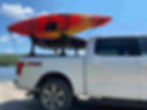 White truck with a red kayak on top, parked by a serene lake under a clear blue sky. FX4 Off Road text on the truck.