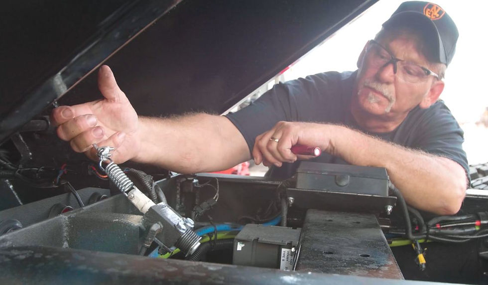 Man in cap and glasses works under a vehicle hood in a focused garage setting