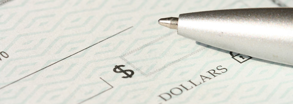 Close-up of a check with a shiny silver pen poised above. The check has a geometric pattern, dollar symbol, and the word "DOLLARS".