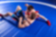 Two young man wrestlers in red and blue uniform wrestling on a blue wrestling carpet in