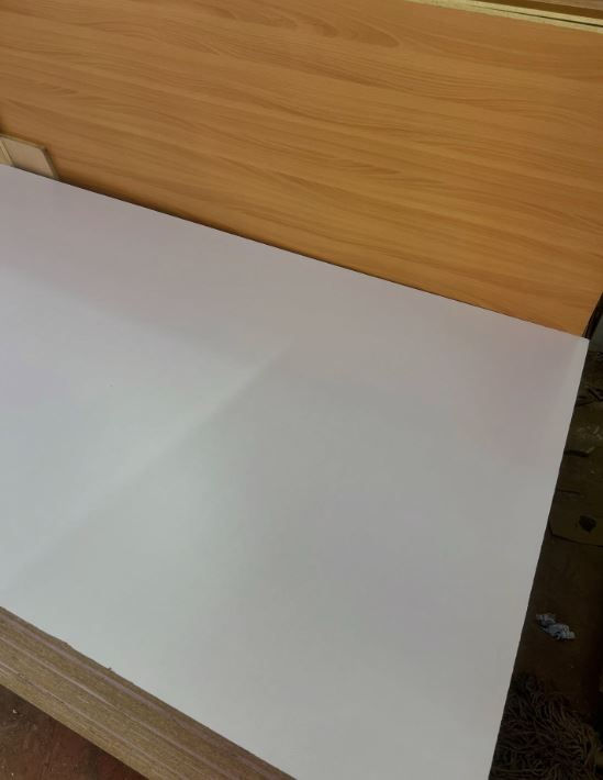 A white sheet on a wood-textured desk with a light brown wall background. No text or significant actions are visible. Quiet, minimal setting.