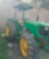 Green John Deere 5075E tractor parked on gravel beside a stone wall. Yellow accents and license plate KTC 4224C visible. Bright daylight.