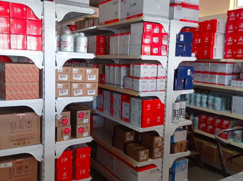 Shelves filled with various boxes, mostly red and white, organized in a storage room. Some containers and bottles are visible.