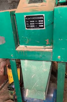 Green industrial Roller Mill and Crusher machine in a workshop setting, with a visible label featuring technical details. Background shows tools and equipment.