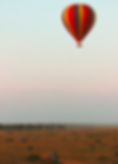 Colorful hot air balloon floats over a savanna at sunrise. A vehicle is on a dirt road below. Serene atmosphere with pastel sky.
