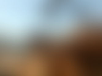 Construction scene with workers on scaffolding, hoisting a large concrete mixer bucket against a clear sky. Urban setting with power lines and buildings.