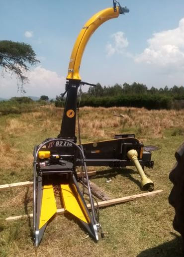 Yellow and black agricultural machine in a grassy field under a blue sky. Large sweeping chute, numbered DT 9212.