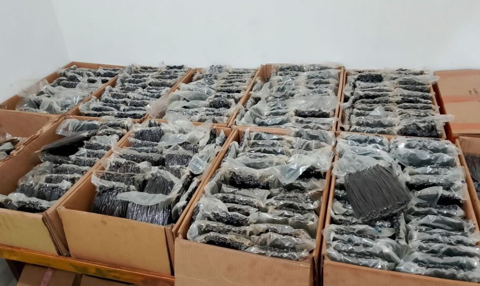 Boxes filled with plastic-wrapped, Vanilla Bean pods components neatly organized on a wooden shelf. The setting is a plain room.