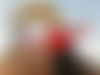 Man in red jacket smiling, arms wide, seated on rocks at Lenana Peak, Mt. Kenya. Sign reads, "Congratulations, Third Highest Peak."