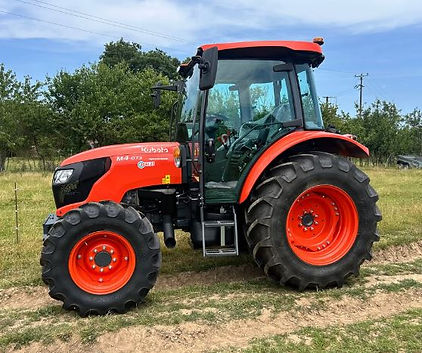 Bright orange tractor with large tires on a grassy field, trees and blue sky in the background, "Kubota M4-073" text on the side.