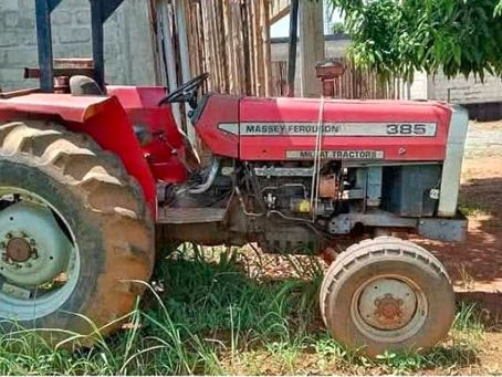 Red Massey Ferguson 385 tractor parked on grass near a building. A plastic chair is in the background under a tree's shade.