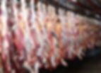 Hanging beef carcasses in a row, in a meat processing facility. Red and white tones dominate the scene, with a metallic background.