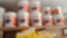 White buckets labeled "Happylick Maziwa" stacked on wooden shelves, with yellow bags below. The setting is a storage or shop area.