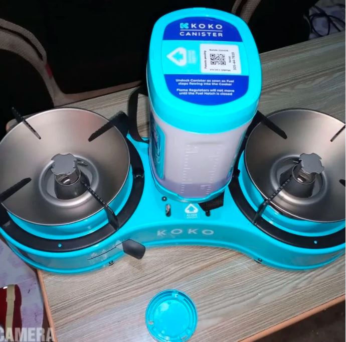 Blue KOKO gas cooker with two burners and a canister on a wooden table. Visible labels and a detached blue lid nearby.