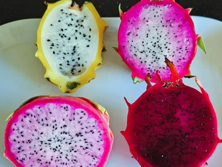 Four dragon fruit halves on a white plate. Two are yellow-skinned with white flesh, and two are pink-skinned with white and red flesh.