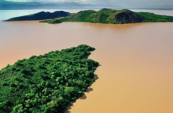 Aerial view of lush green islands in a muddy brown lake baringo , surrounded by distant hills under a clear sky. Calm and serene landscape.