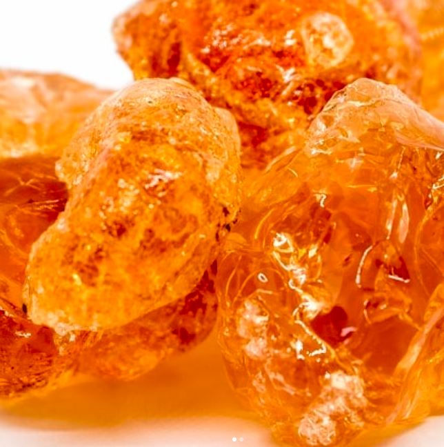 Close-up of shiny, translucent acacia seyal gum arabic with rich orange hues, capturing their textured, glossy surfaces.