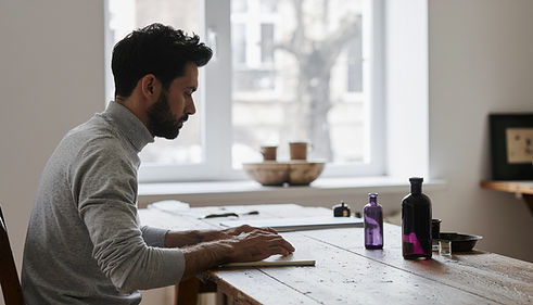 Christian Jungnickel arbeitet in einem minimalistischen Atelier an strukturierten Raum- und Signaturkonzepten, violette Glasflaschen auf einem Holztisch, ruhige architektonische Umgebung.