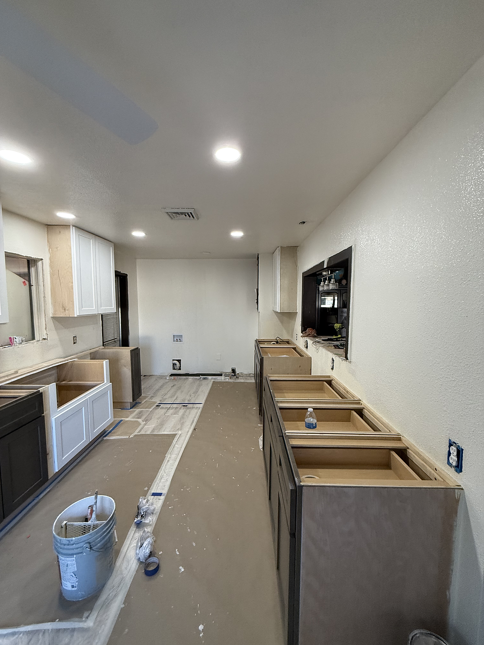Kitchen under renovation with bare cabinetry, brown paper covering the floor, paint supplies in a gray bucket, and recessed lighting above.