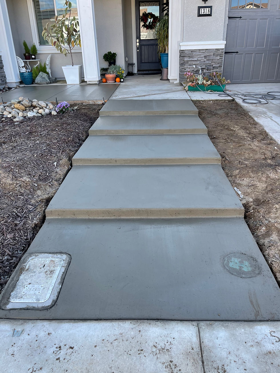 Finished concrete walkway and steps leading from the sidewalk to the front porch of a home, with landscaping and driveway areas on both sides.