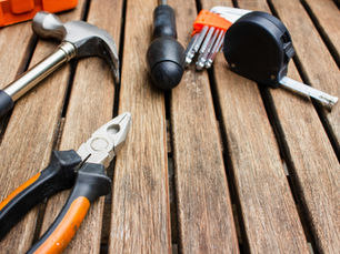 Hammer, pliers, tape measure, and screwdriver bits laid on a wooden table, suggesting DIY repair work.