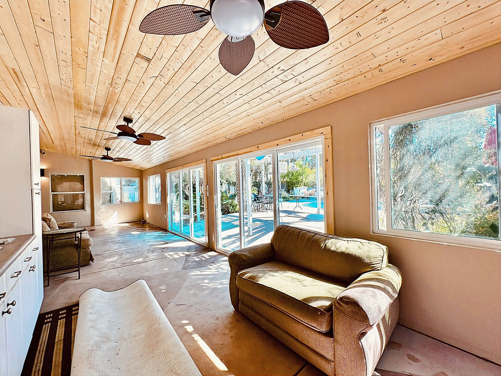 Sunlit patio room with wood plank ceiling, ceiling fans, sofa, and large windows overlooking a bright pool and patio area