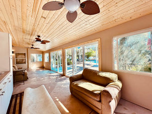 Sunlit patio room with wood plank ceiling, ceiling fans, sofa, and large windows overlooking a bright pool and patio area