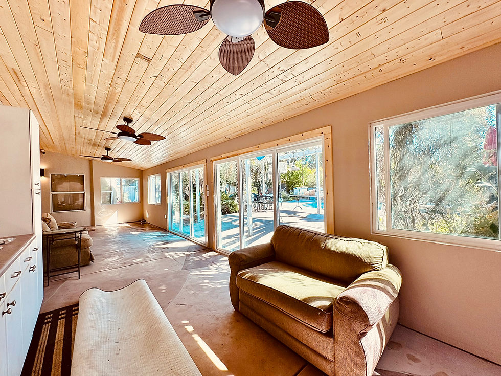 Sunlit patio room with wood plank ceiling, ceiling fans, sofa, and large windows overlooking a bright pool and patio area