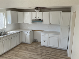 After kitchen remodel with white shaker cabinets, white subway tile backsplash, light wood-look flooring, new countertops, and a brighter updated layout.