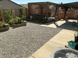 Residential backyard featuring a wood pergola, raised planter boxes, gravel landscaping, and a shaded patio space.