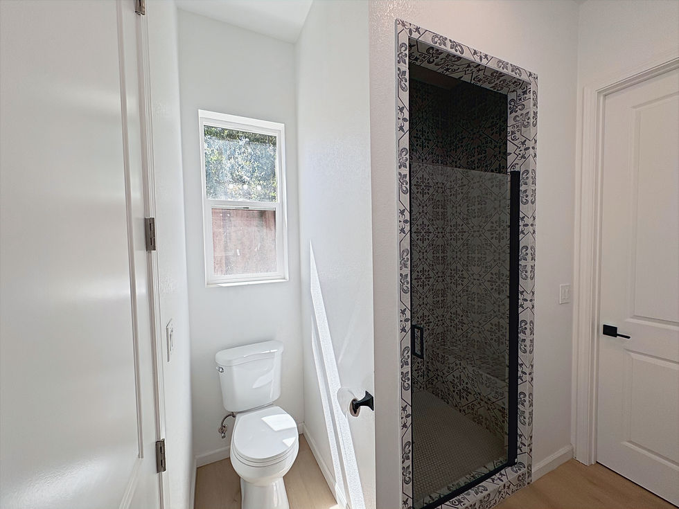 Completed bathroom with a toilet beneath a narrow window and a patterned walk-in shower enclosed by a black-framed glass door.