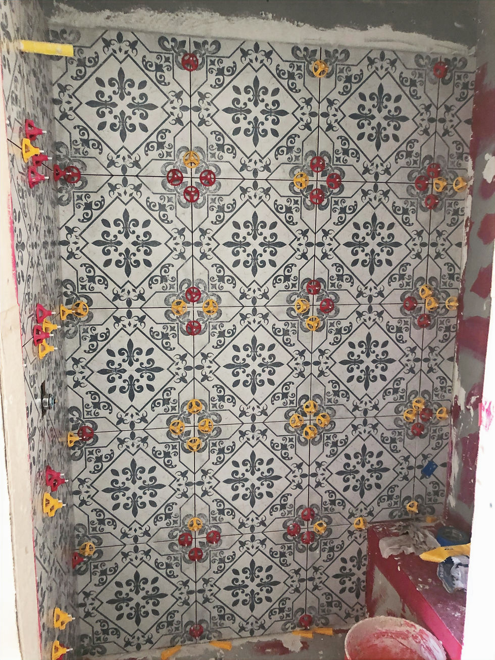Walk-in shower under construction with black-and-white patterned wall tile held in place by red and yellow leveling spacers.