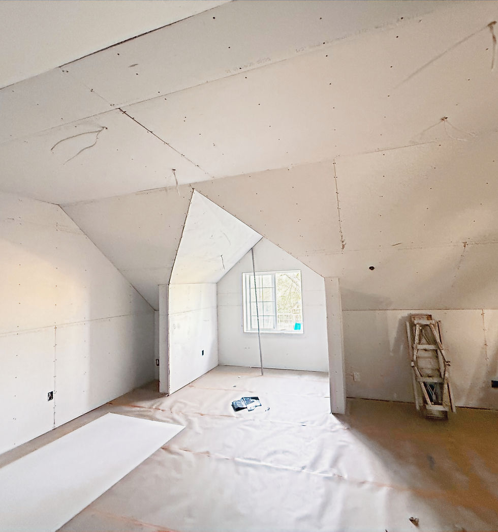 Interior home remodel in progress with new drywall, sloped ceilings, unfinished walls, protected flooring, and a window bringing in natural light.