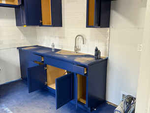 Kitchen remodel in progress featuring deep blue cabinets, a white subway tile backsplash, a stainless steel faucet, and protected floors and countertops.