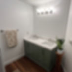 Bathroom remodel with green double vanity, marble-look countertop, two sinks, modern light fixture, shiplap accent wall, and wood-look flooring.