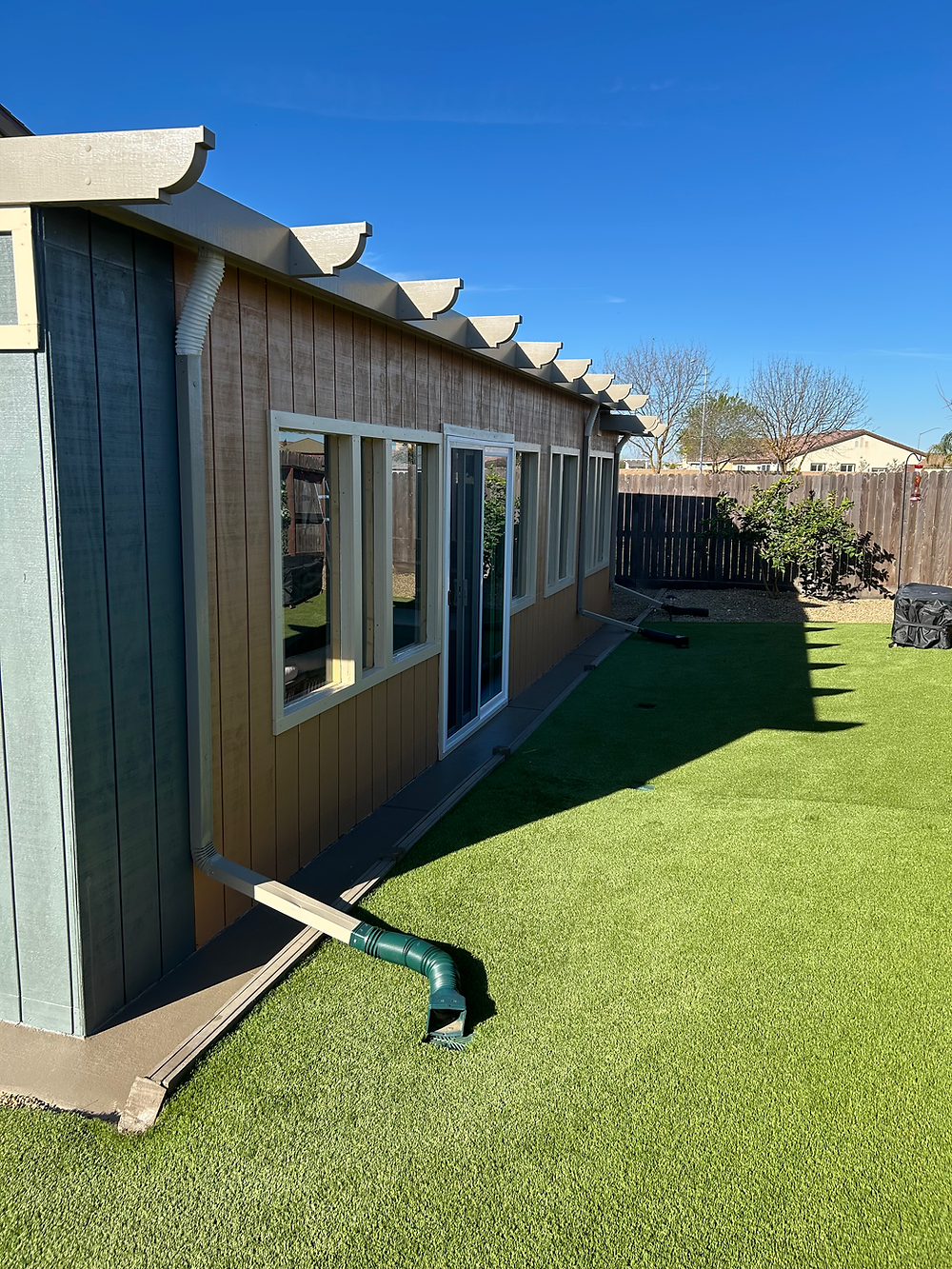 Exterior view of an enclosed patio addition with windows, sliding glass door, siding, and backyard lawn.