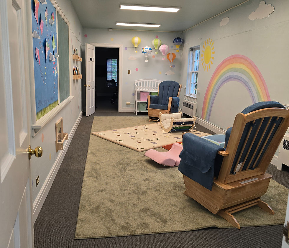 Nursery room with blue chairs, a crib, and colorful decor including a rainbow mural, hot air balloons, and kites. Books on shelves.