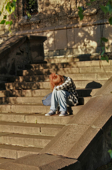 girl sitting with head down, sad, on steps outdoors